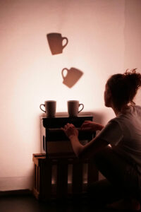 La comédienne joue d'un petit piano en dessous de deux ombres de tasses.