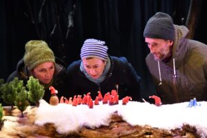 Les trois comédiens sont habillés en tenue d'hiver et regardent les lutins rouges.