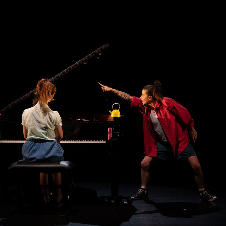 La comédienne est à côté du piano et pointe du doigt le ciel.